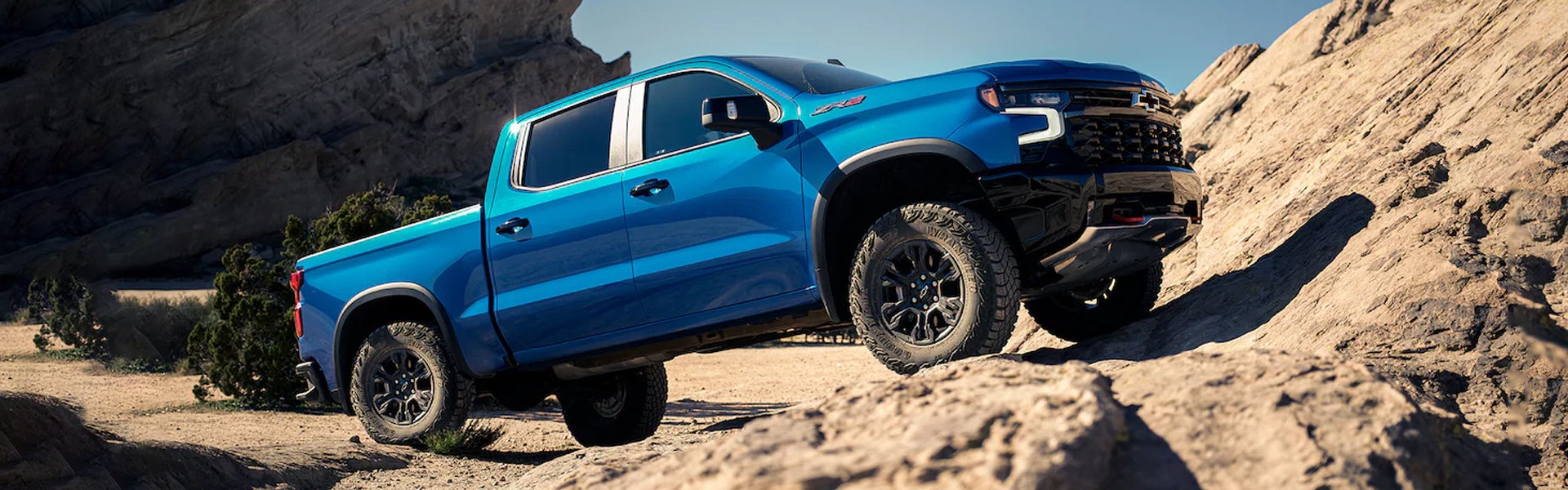 blue 2023 Chevrolet Silverado 1500 on a rugged, dusty mountain trail, showcasing its strength and durability.