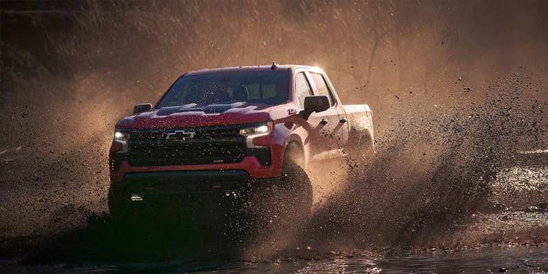 2023 Chevy Silverado 1500 driving through a muddy path, showcasing its off-road capability.