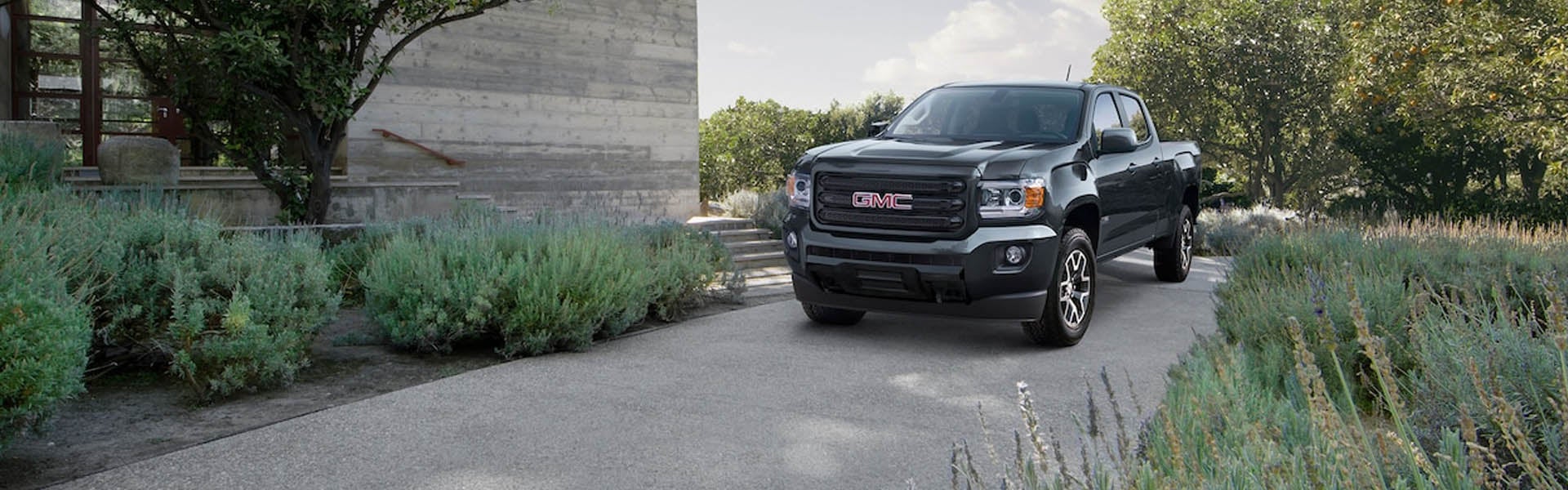 2019 GMC Canyon parked, surrounded by green plants and trees, blending into the natural landscape.