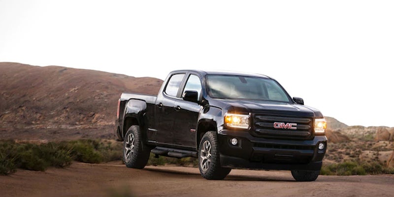 A black GMC Canyon driving on a dusty area, with a dusty mountain in the background.