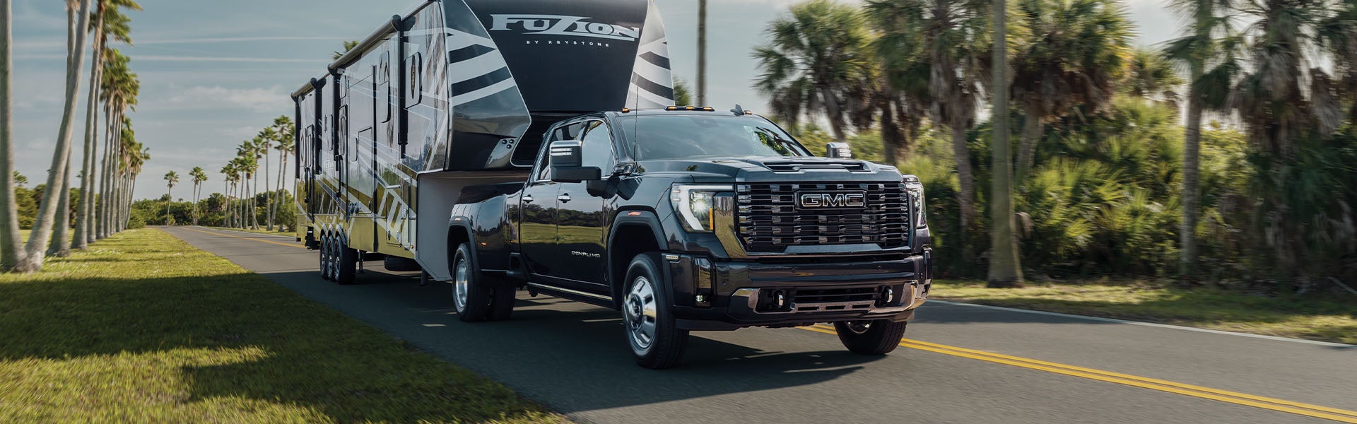 GMC Sierra HD towing a black container on the road, with trees lining the roadside.