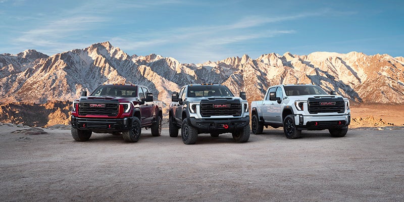 Three GMC Sierra HD trucks parked in front of a mountain range.