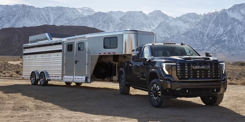 A black GMC Sierra HD pickup truck towing a large white trailer in front of a mountain range.