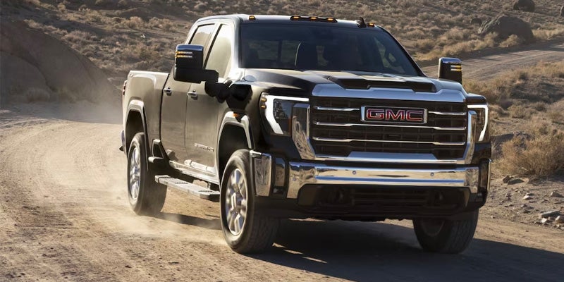 A black GMC Sierra HD pickup truck driving on a dusty road in a desert-like environment.